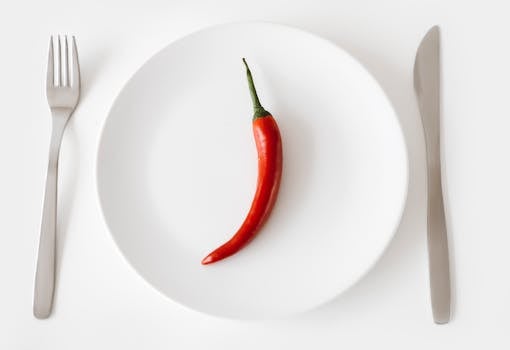 pexels-photo-7214831-7214831 A single red chili pepper on a white plate with fork and knife, embodying simplicity and spicy flavor.